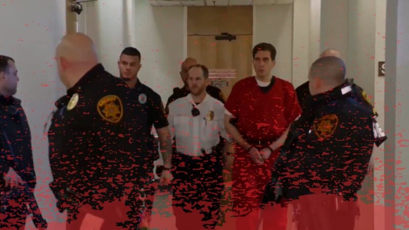 A Man in A Red Prison Jumpsuit Is Escorted by Five Police Officers Through a Corridor